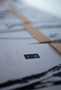 Person comparing textured and smooth art papers beside a vibrant print on a table indoors
