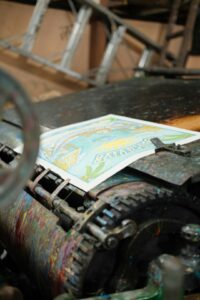 A person wearing white gloves frames a colorful art print using a wooden frame and protective glass.