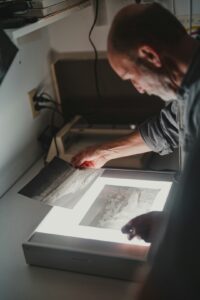 A person at a desk adjusts color on a digital art file displayed on a computer monitor.