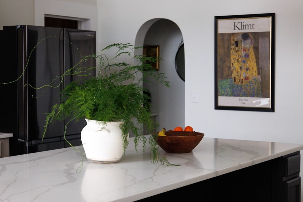 Person carefully hanging a framed art print on a living room wall above a wooden sideboard