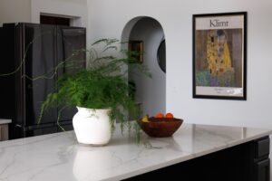 Person carefully hanging a framed art print on a living room wall above a wooden sideboard