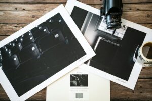 Hands examine a detailed art print beside cotton paper, pigment ink samples, and archival mat board.