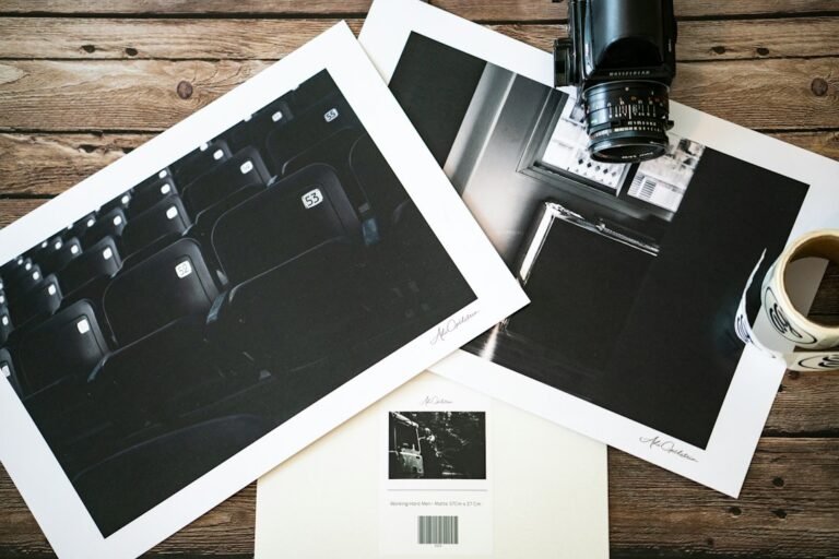 Hands examine a detailed art print beside cotton paper, pigment ink samples, and archival mat board.