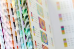 Artist compares a calibrated monitor with a test print beside labeled fine art paper samples.