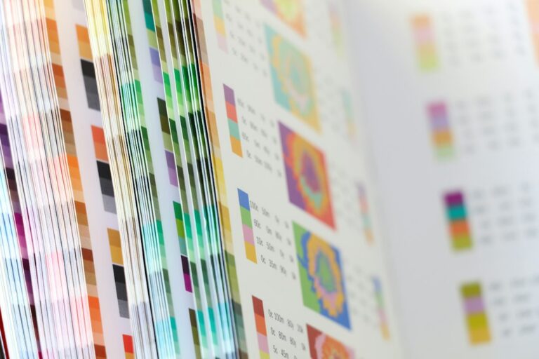 Artist compares a calibrated monitor with a test print beside labeled fine art paper samples.