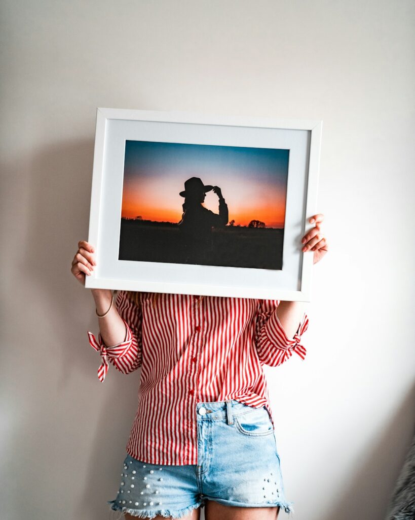 Person measuring a framed fine art print above a console table with paper templates on the wall
