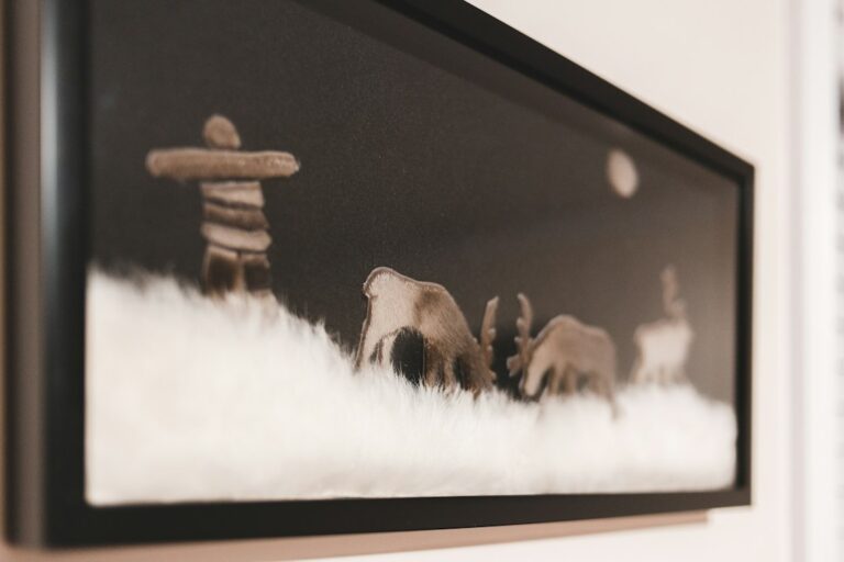A person compares a textured canvas print with a framed paper artwork on a well-lit worktable.